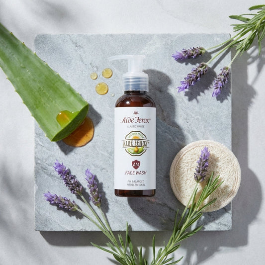Aloe Ferox face wash bottle with aloe ferox leaf, lavender flowers, and soap bar on a marble surface.