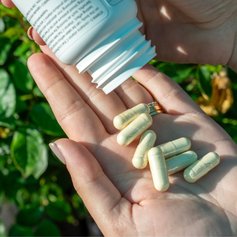 Hand holding capsules with a bottle of supplements against a natural Aloe Ferox background