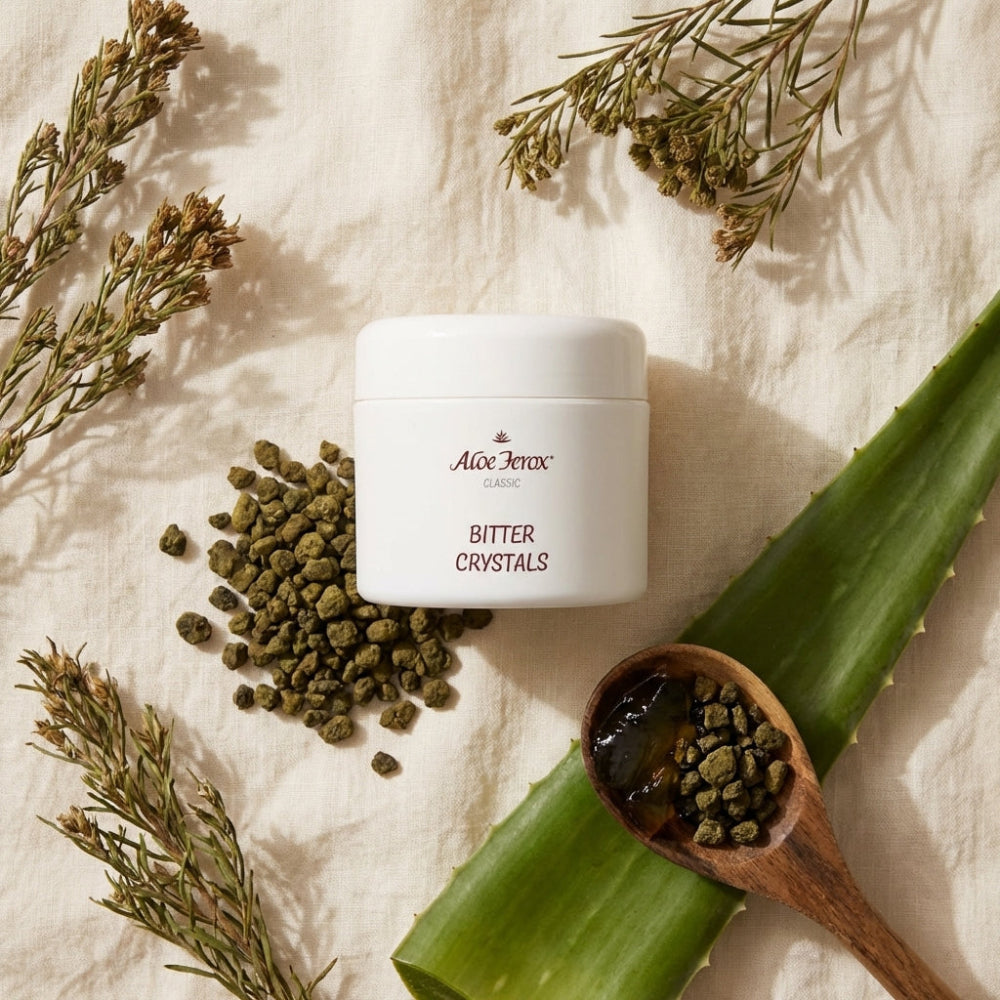 A container of Aloe Ferox Bitter Crystals with aloe ferox leaf and herbs on a light background