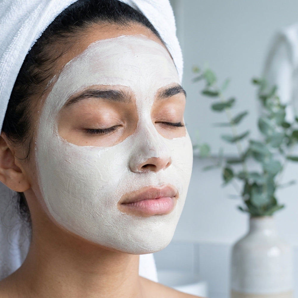 Woman applying aloe ferox facial mask with a blurred indoor background